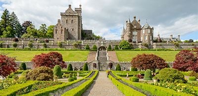 Impressive gardens with green and red trees lining a path up to a group of building 