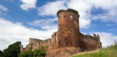 The ruins of Bothwell Castle against a cloudy blue sky 