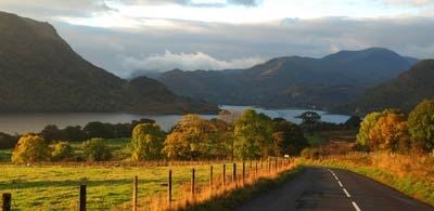 A road leading the calm water of Kendal lake, surrounded by trees and hills