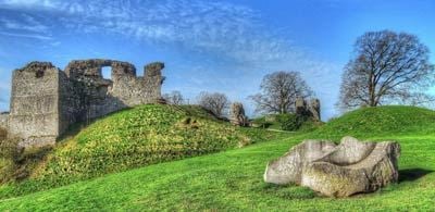 the ruins of Kendal castel sit on a vribate green grass field with bare winter trees in the background