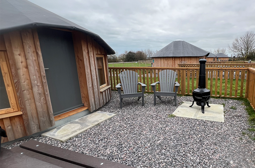 wooden yurt with outdoor seating area and fire pit.