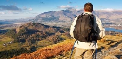 a man wearing a backpack enjoys the view from atop The Old Man of Coniston