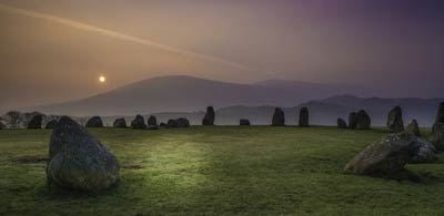 a moody sunrise casts light on stones at Castlerigg stone circle