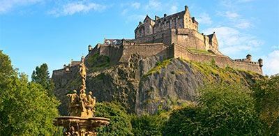 Edinburg Castle sitting at the top of a steep rocky hill surrounded by trees