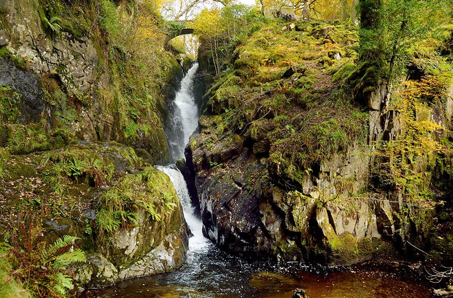 Cascading waterfall Aira Force lined by jagged grassy rocks 