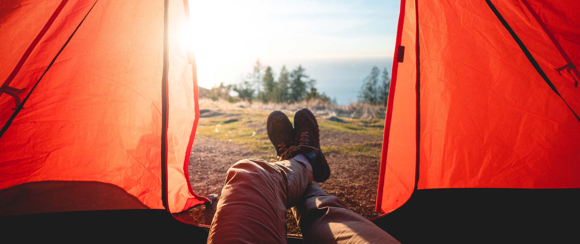 Trainers on feet protruding from an orange tent in the warm sunshine, overlooking trees