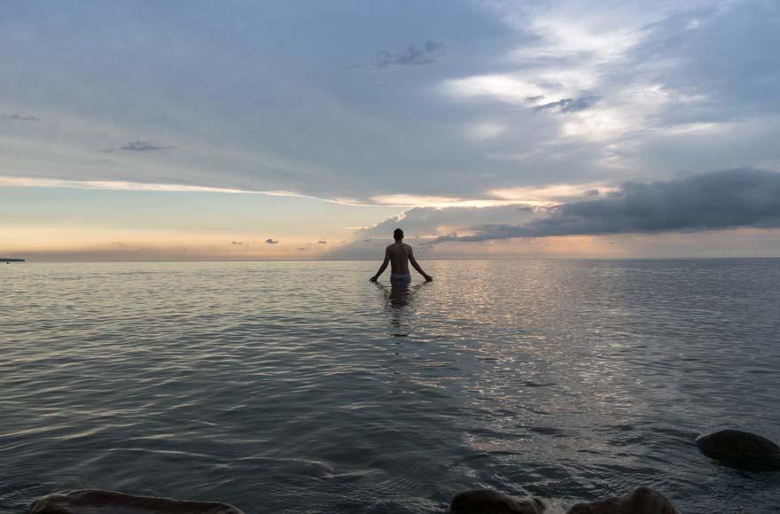 Man venturing out into open water, with sun beaming through clouds in the sky