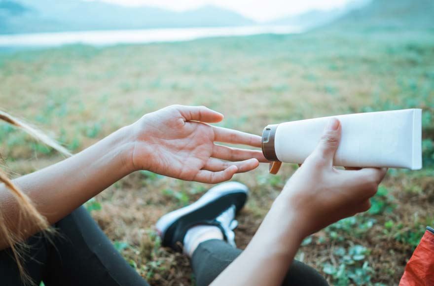 Person sitting in a field applying cream to their hand