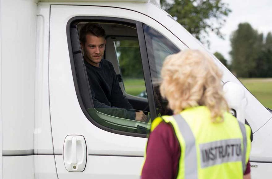 A man sits in the drivers seat of a mototrhome and talks to a a female instructor wearing a high visibility jacket