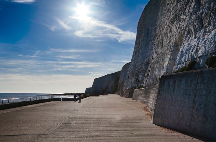 Large cliffs loom over the undercliff walk in Saltdean, against a sunny blue sky