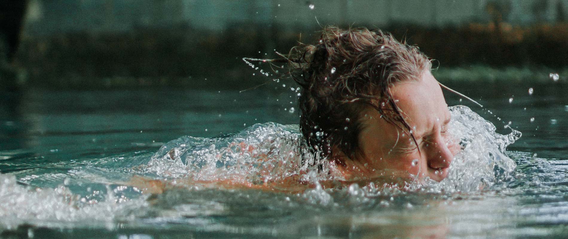 Boy swimming in a lake, with head emerging from the surface of the water 