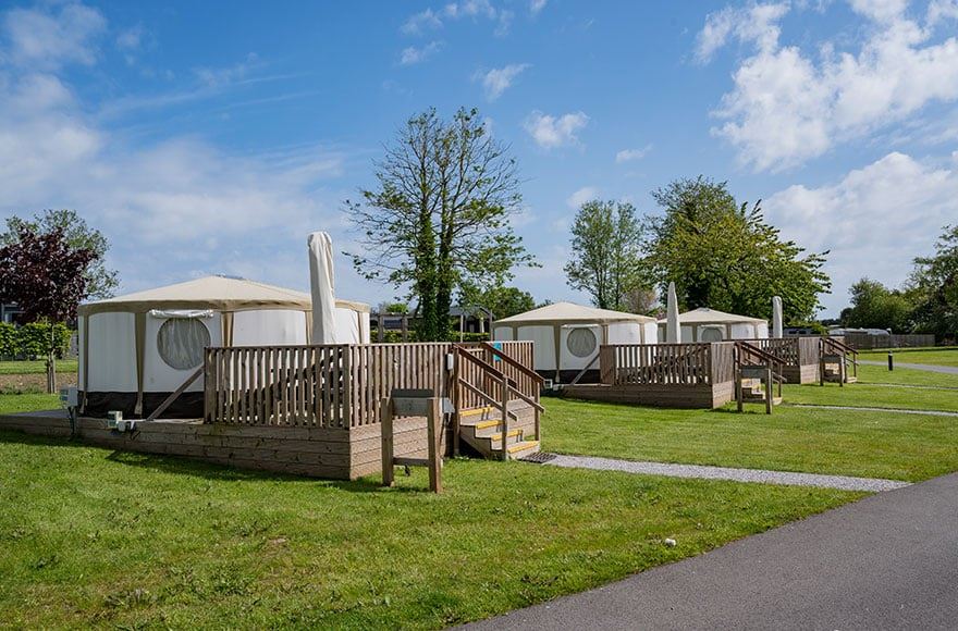 3 canvas yurts with outdoor decking surrounded by grass on a backdrop of trees