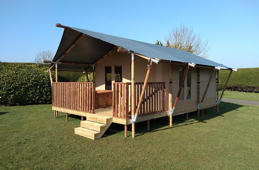 A safari tent with a pitech roof and rustic decking on grass with a hedge boarder