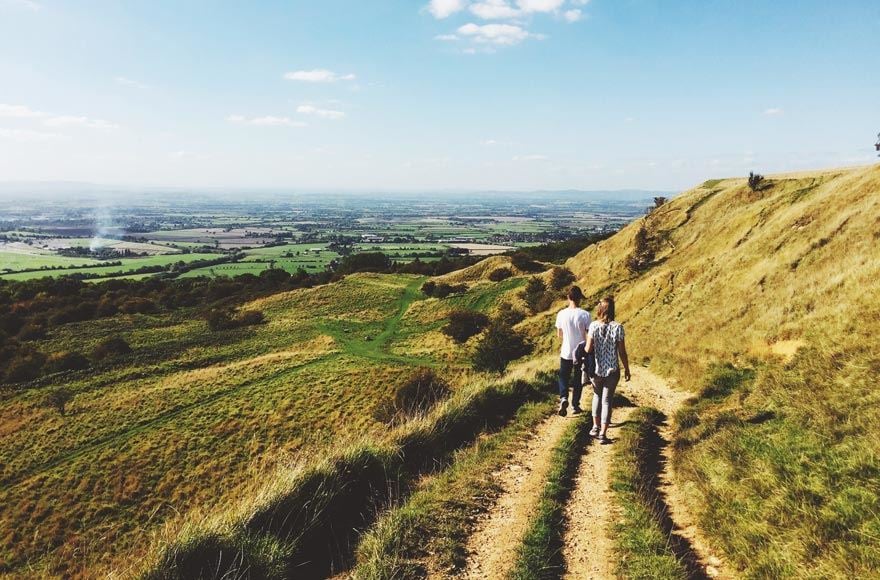 A couple walk down a track along the Cotswolds Way showcasing the vast green landscape