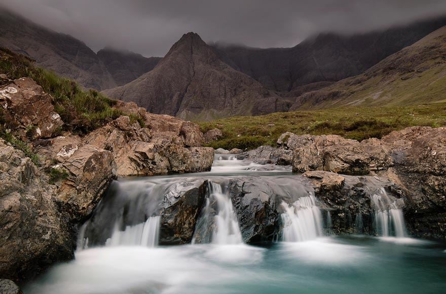 Rushing water runs down the fairy pools with majestic moody hills in the background