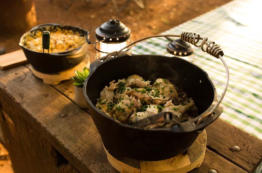 An iron pan with a warming pasta dish  sitting on a wooden bench