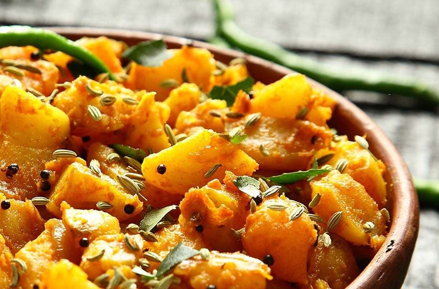 A bowl of curry with mushrooms and potato topped with seeds 