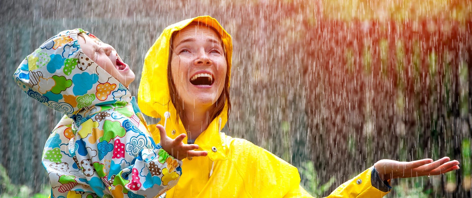 Mother and daughter playing in the rain wearing colourful raincoats