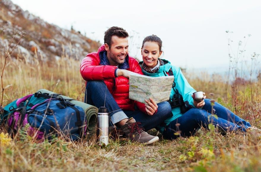 Couple sat down with backpacks reading a map in rural setting