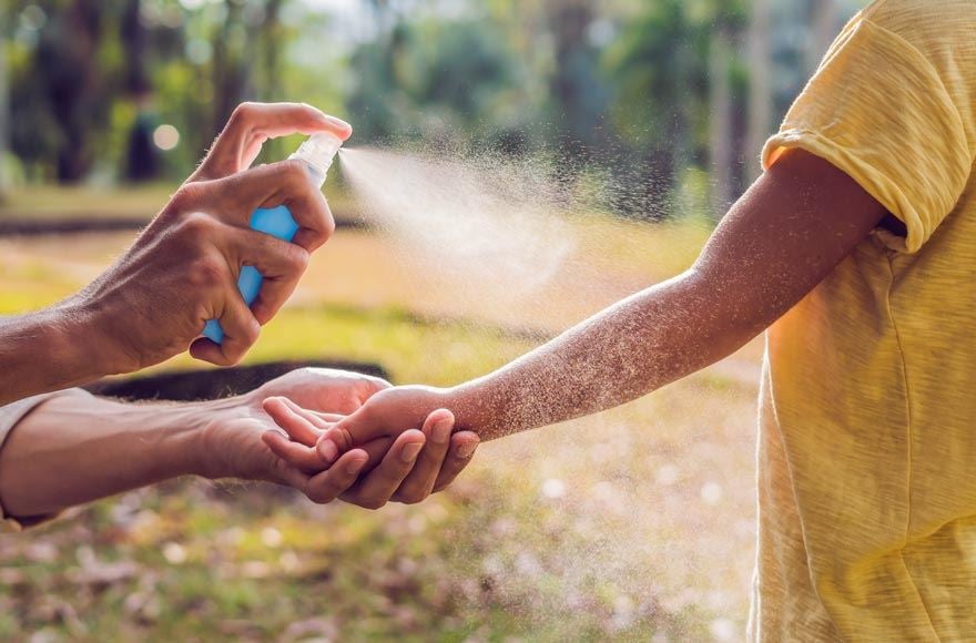 A parent sprays their child's arm with inspect repellent 