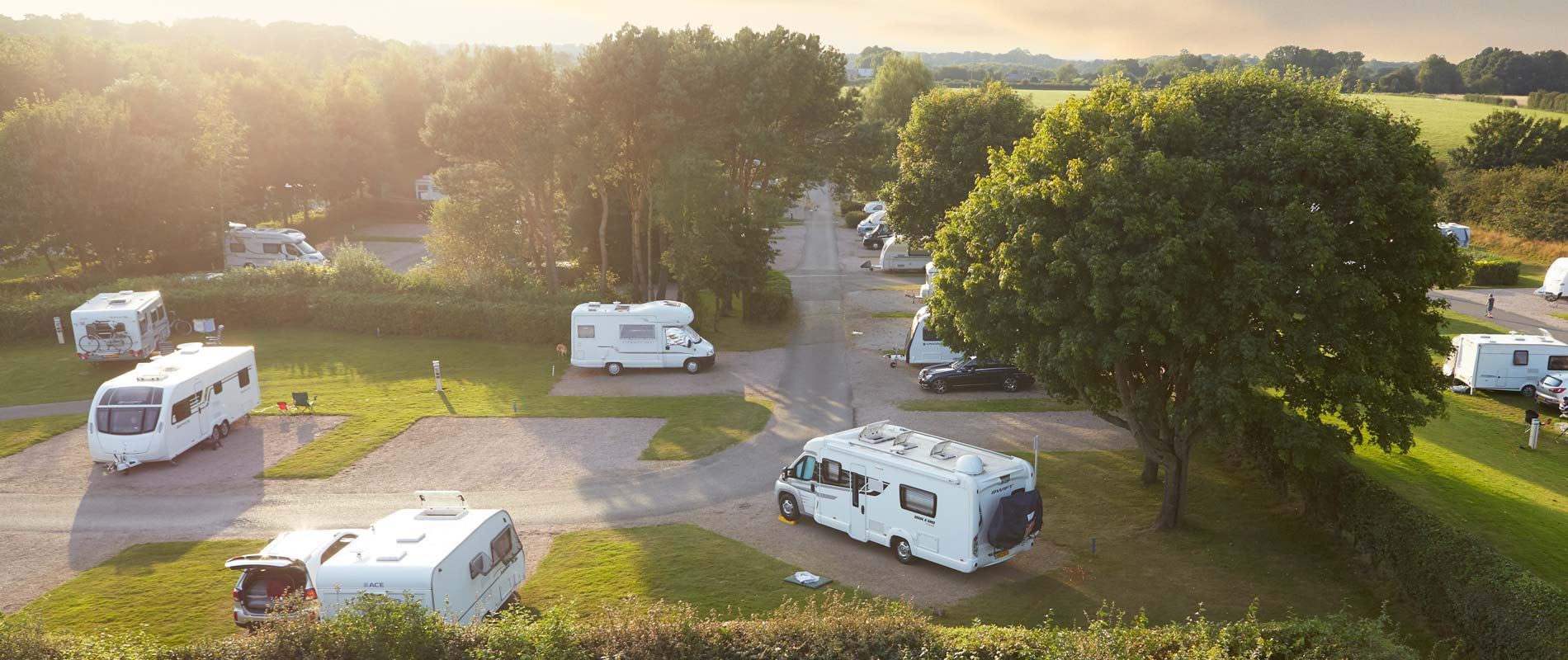 caravans and motorhomes pitches on gravel pitches surrounded by grass and trees at Black Horse Farm Campsite