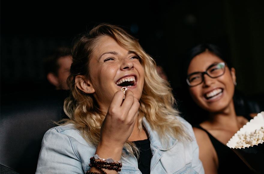 Two friends laughing and eating popcorn at the theatre