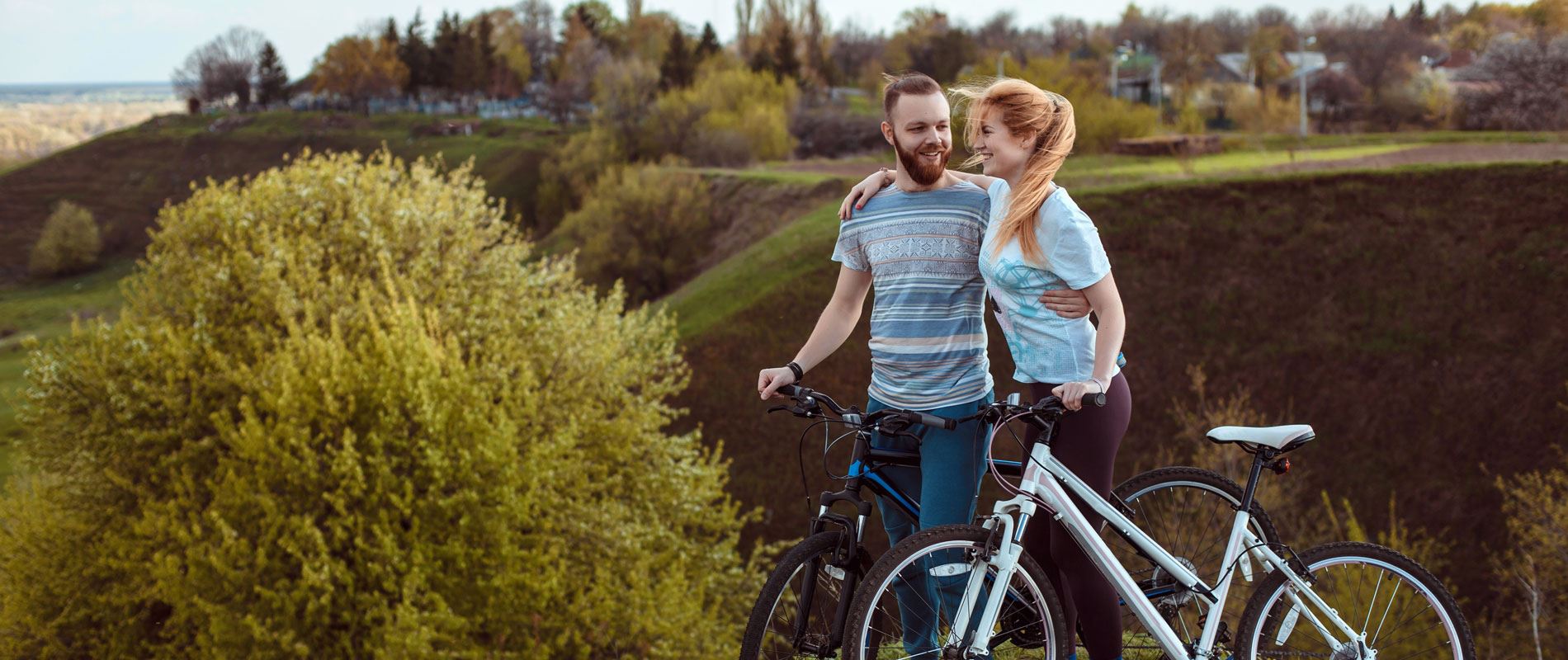 A couple embrace next to their bikes against a backdrop of beautiful forest landscape