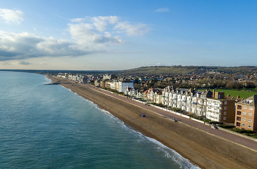 Kent coast line with sandy beach and calm sea waters lined by tall white buildings 