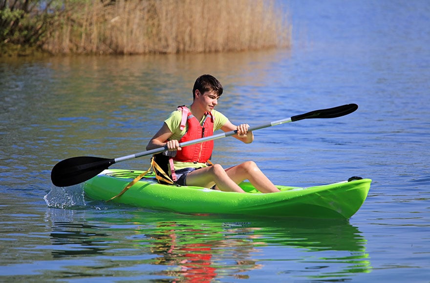 a young man wearing a lifejacket kayaks in a green kayak on open water