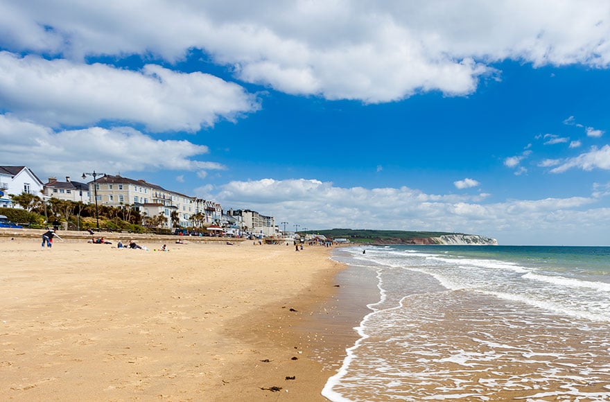 sandy beach with waves lapping the shore against a cloudy blue sky 