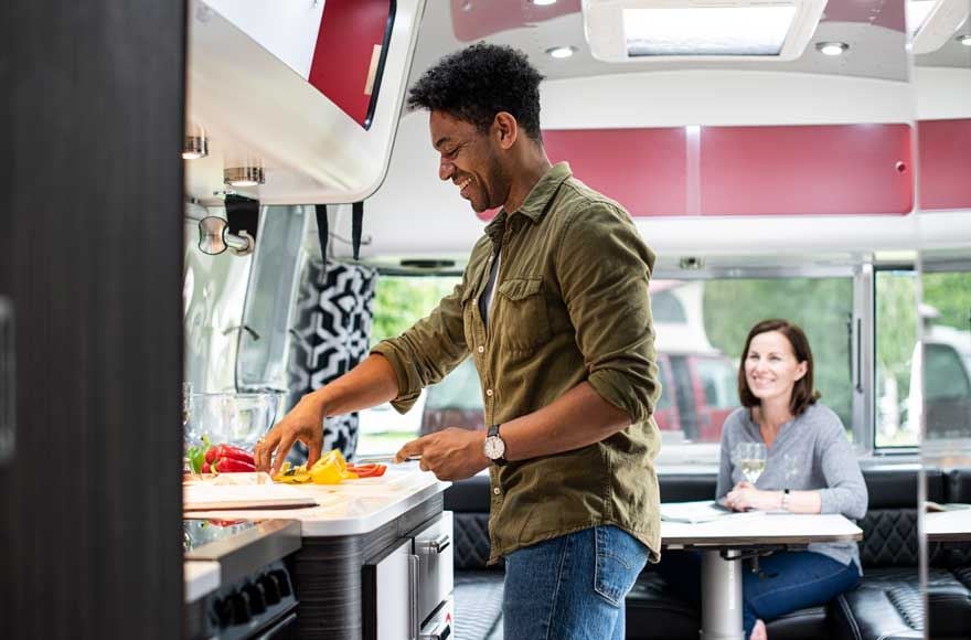 Man cooking in airstream kitchen while chatting to a woman