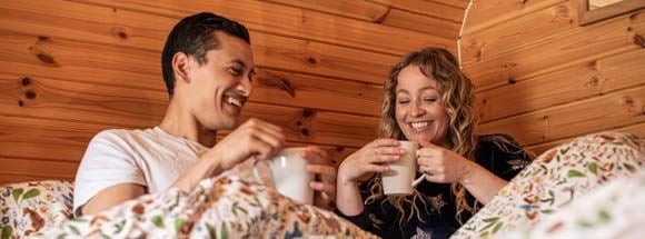 Couple under duvet in wooden-interior glamping pod