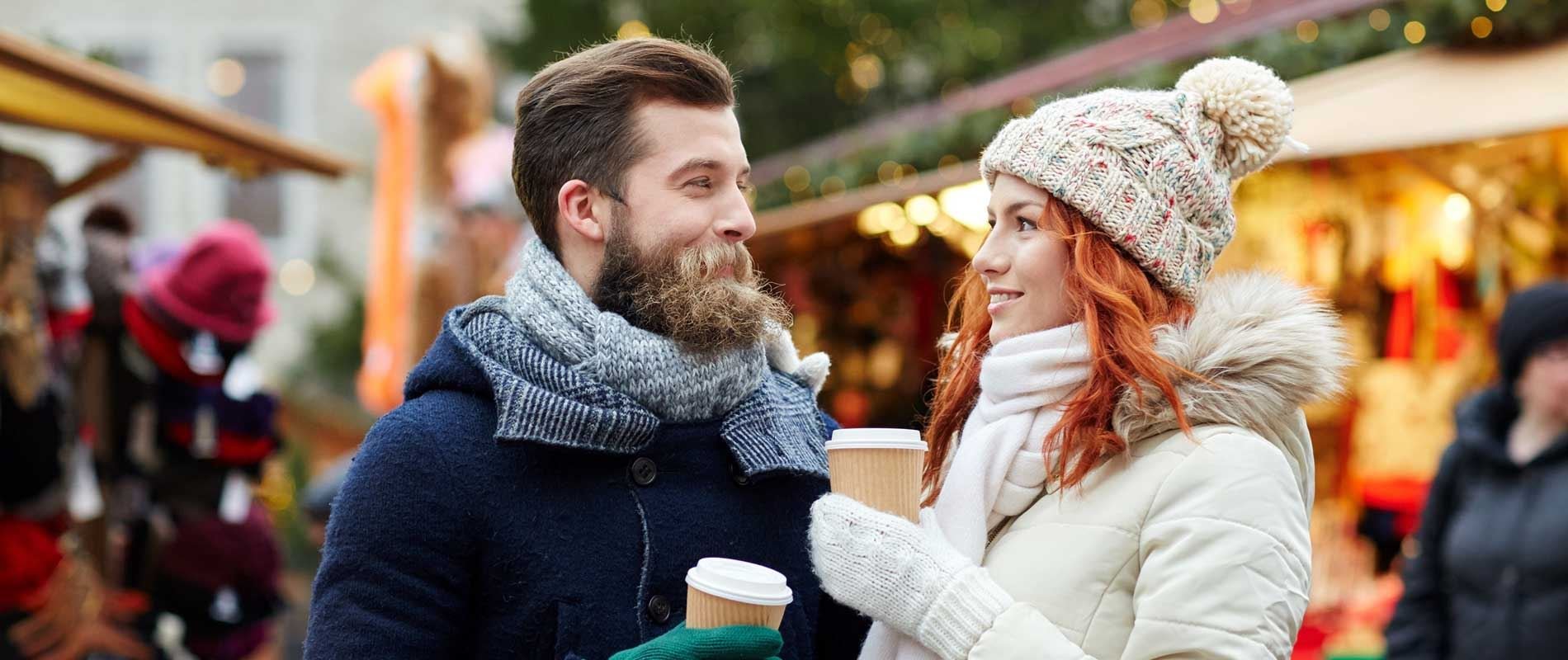 a couple wrapped up for the cold winter weather in hats, coats and scarves enjoying a hot drink