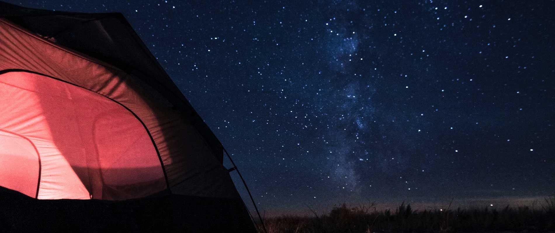 A red tent illuminated against a dark star filled sky 