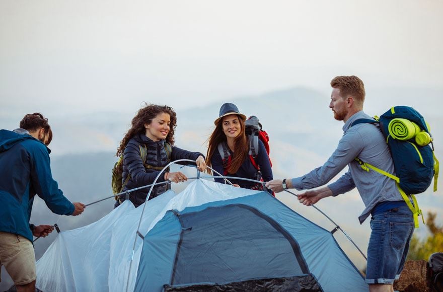 Four friends putting up a blue four-man tent