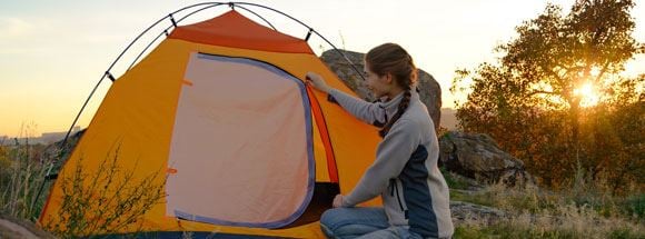 Girl putting up a tent surrounded by nature