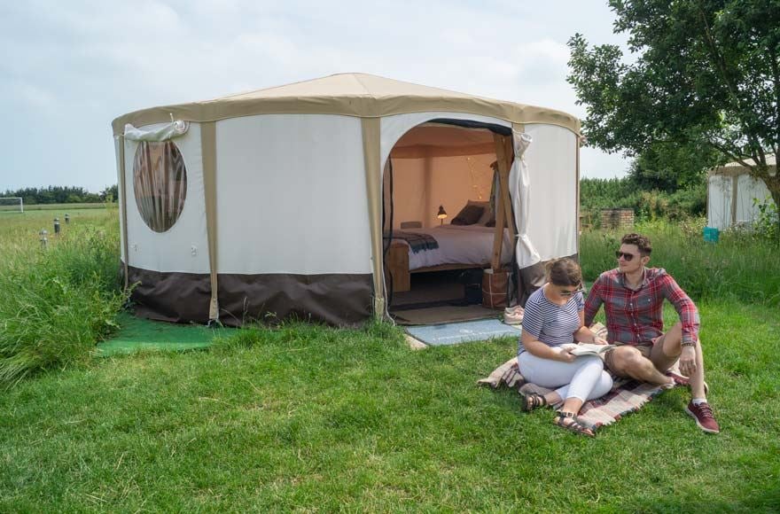 Couple sitting on blanket outside a canvas yurt at the Experience Freedom Daleacres campsite in Kent