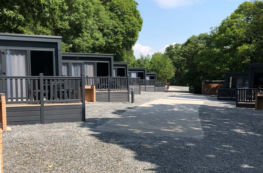 a row of glamping pods with outdoor decking against a backdrop of tress 