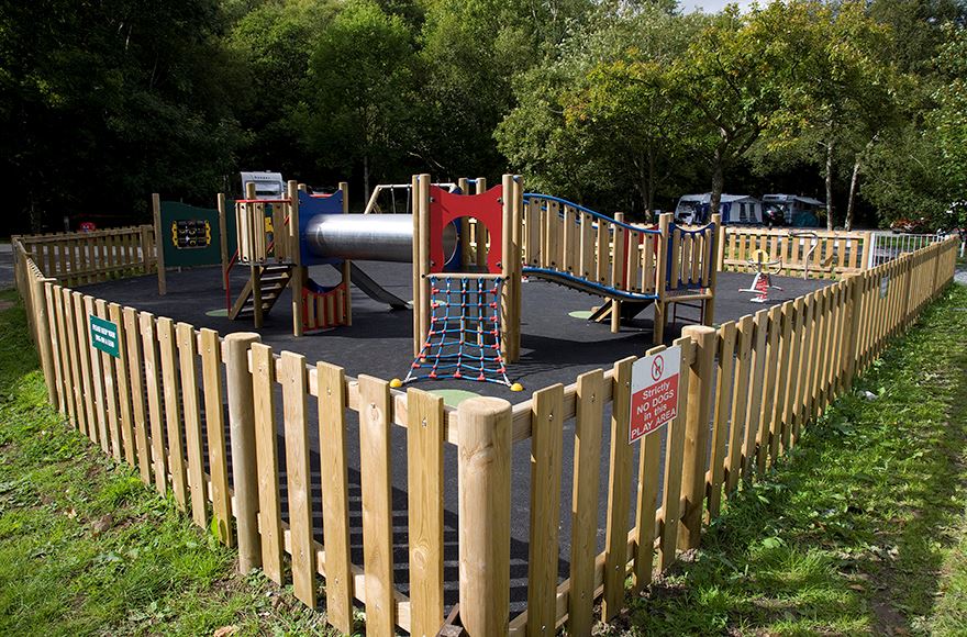 Childrens playground with colourful clibing frame enclosed by a wooden fence