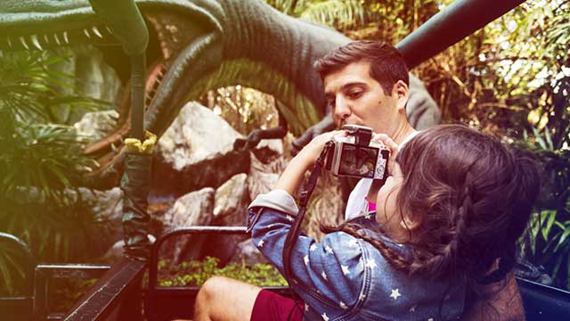 A man holds up a little girl to take a photo in the Dinosaur Park