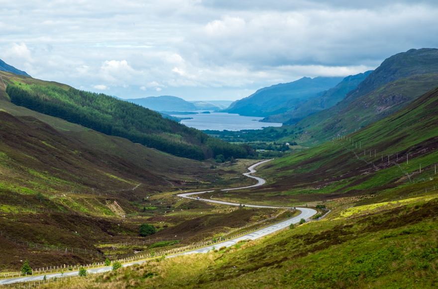 Winding road going down through the valley with Loch Maree and mountains in the distance