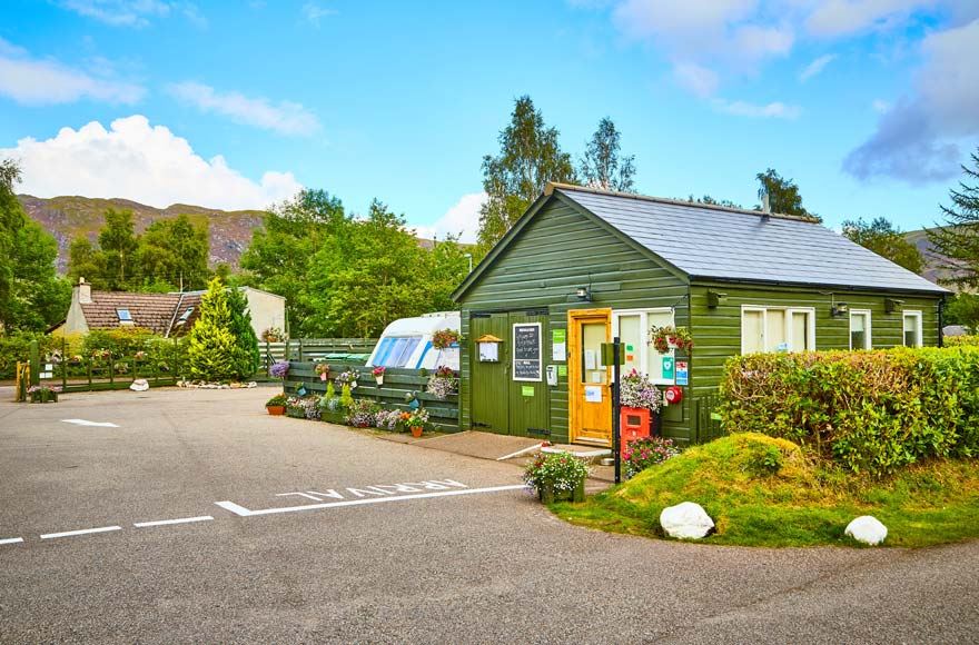 Tarmac arrival area with green wooden reception building, with house and caravan and tress in the background