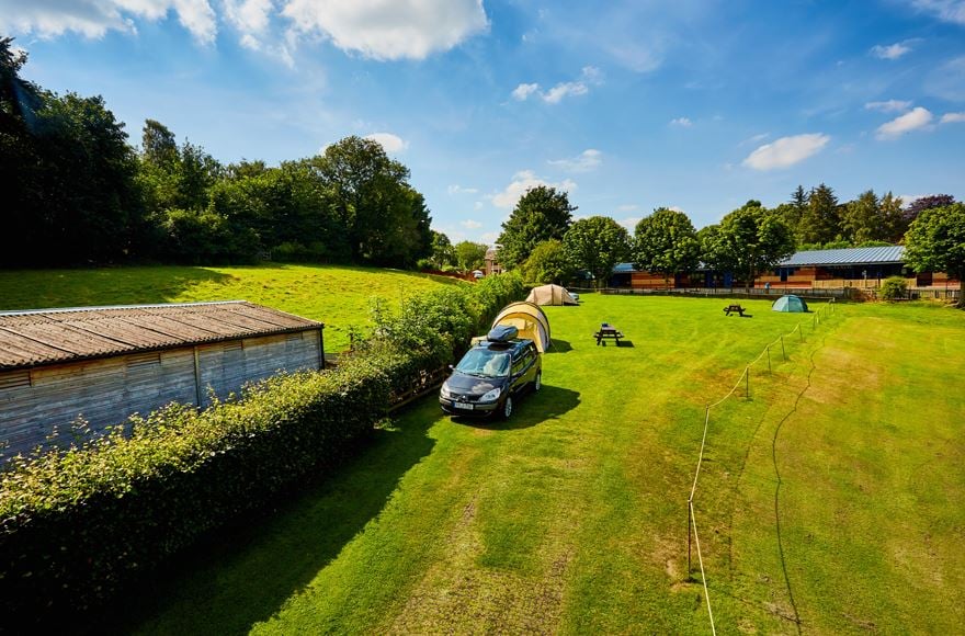 Camping field with tents pitches next to the hedge row  dividing from a hilly fieldblue sky