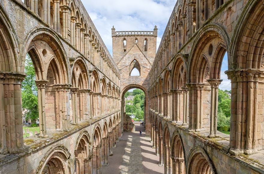 Internal view of Jedburgh Abbey ruins from second level with the arched window frames on either side all the way to the entrance