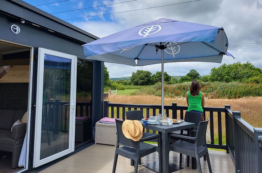 A woman looks over a field of crops from the decking of her glamping pod