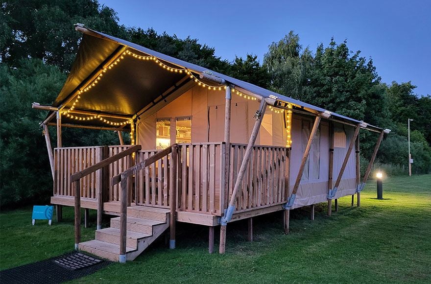 A safari tent on grass decorated with fairy lights