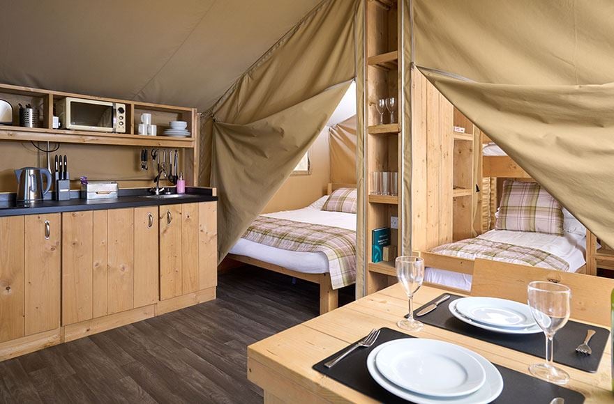 Interior of a safari tent shwoing dining table and two bedrooms 