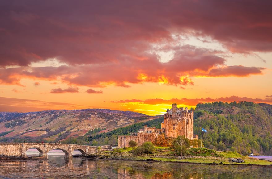 Eilean Donan castle view from across the loch with the stone bridge. Beautiful sunset behind the castle  and the mountains with orange and pinkish 