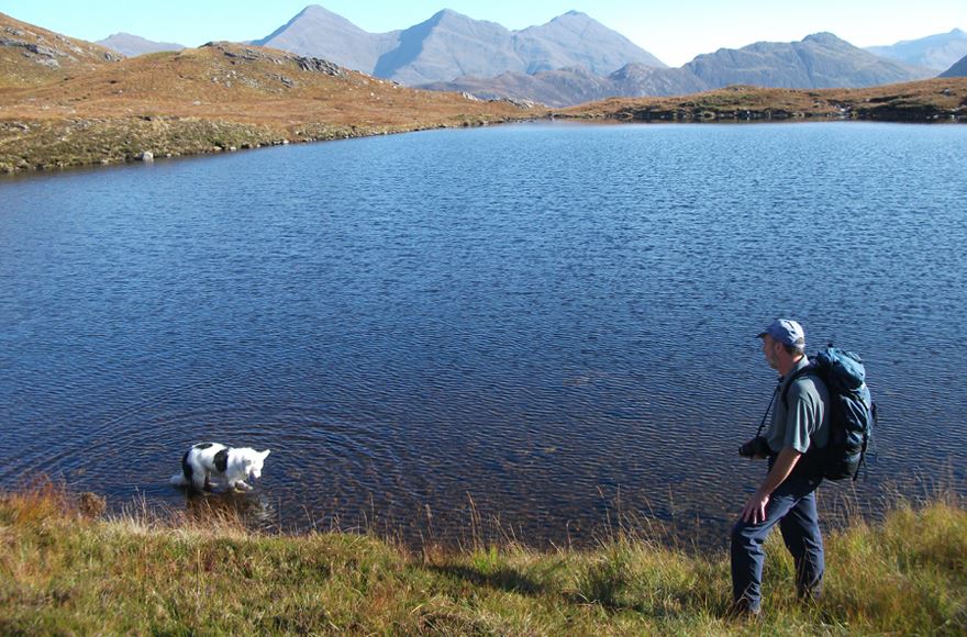 Hiker watching his collie dog in the Sparkling waters of Glen Shiel which spreads all the way back to the mountains