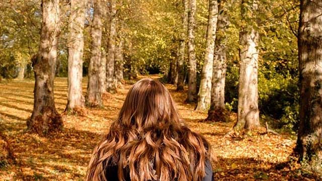 Person with long auburn hair looking down a pathway lined with trees with autumn colours